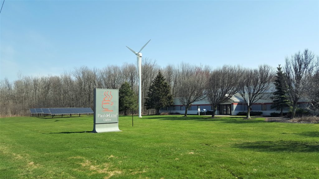 A wind turbine and solar photovoltaic array provide renewable energy for the Paul deLima Coffee roasting facility.