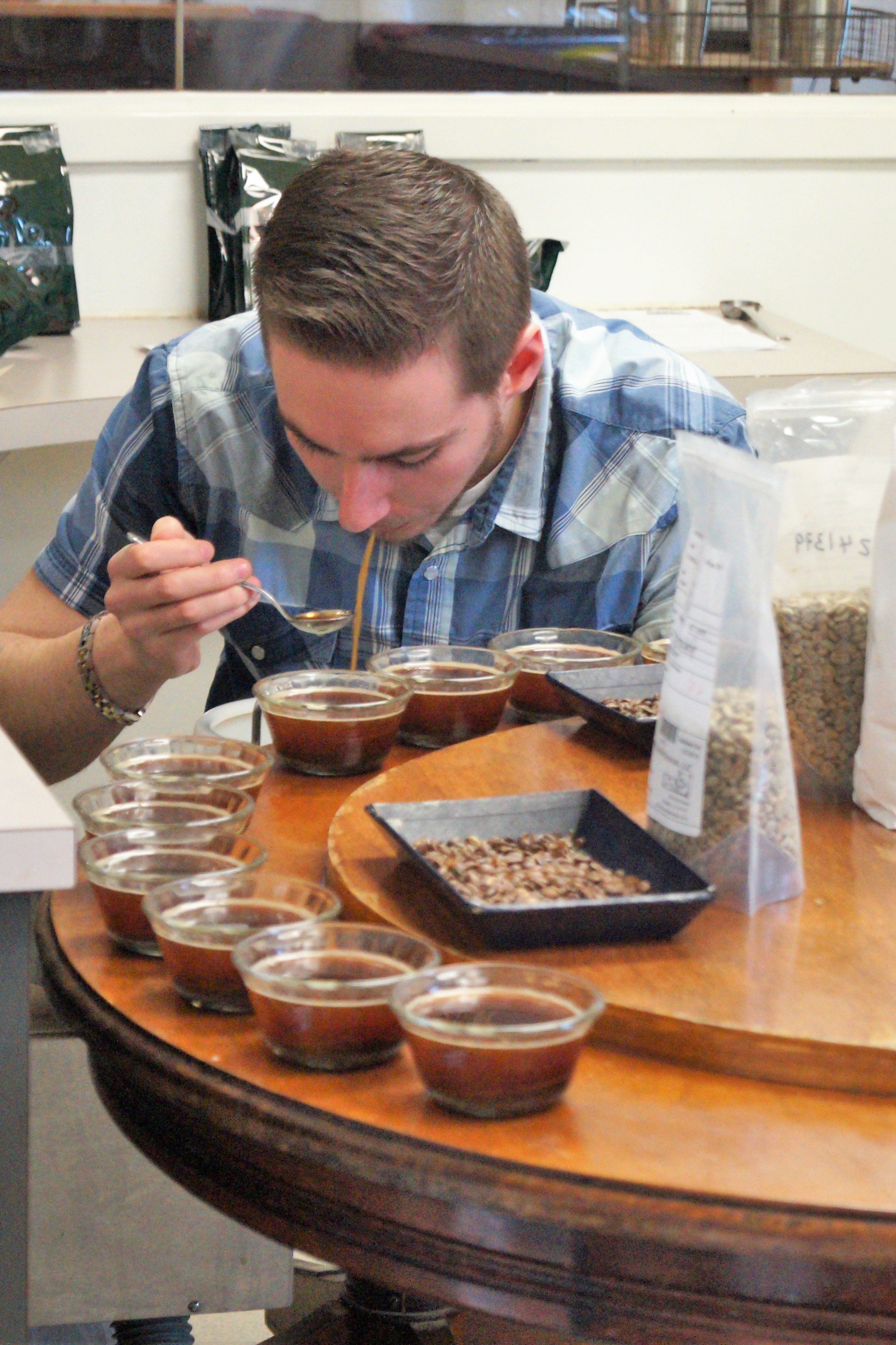 Ryan cupping the coffee samples as the third taster in series. The cuppers don't ingest the concentrated coffee and here he spits the coffee into the dentist spittoon after having tasted it.